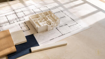 Ivory architectural model over a floor plan with a scale ruler and material samples, illustrating circulation and spatial review.
