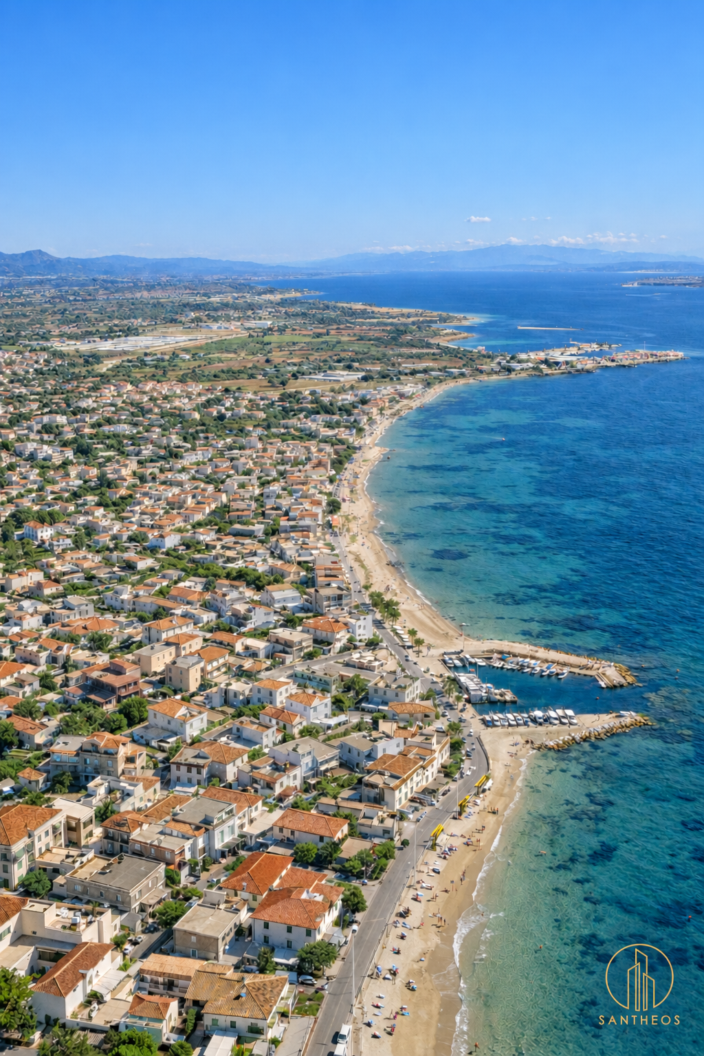 Aerial view of a sandy coastline, waterfront road and low-rise homes beside the blue sea.